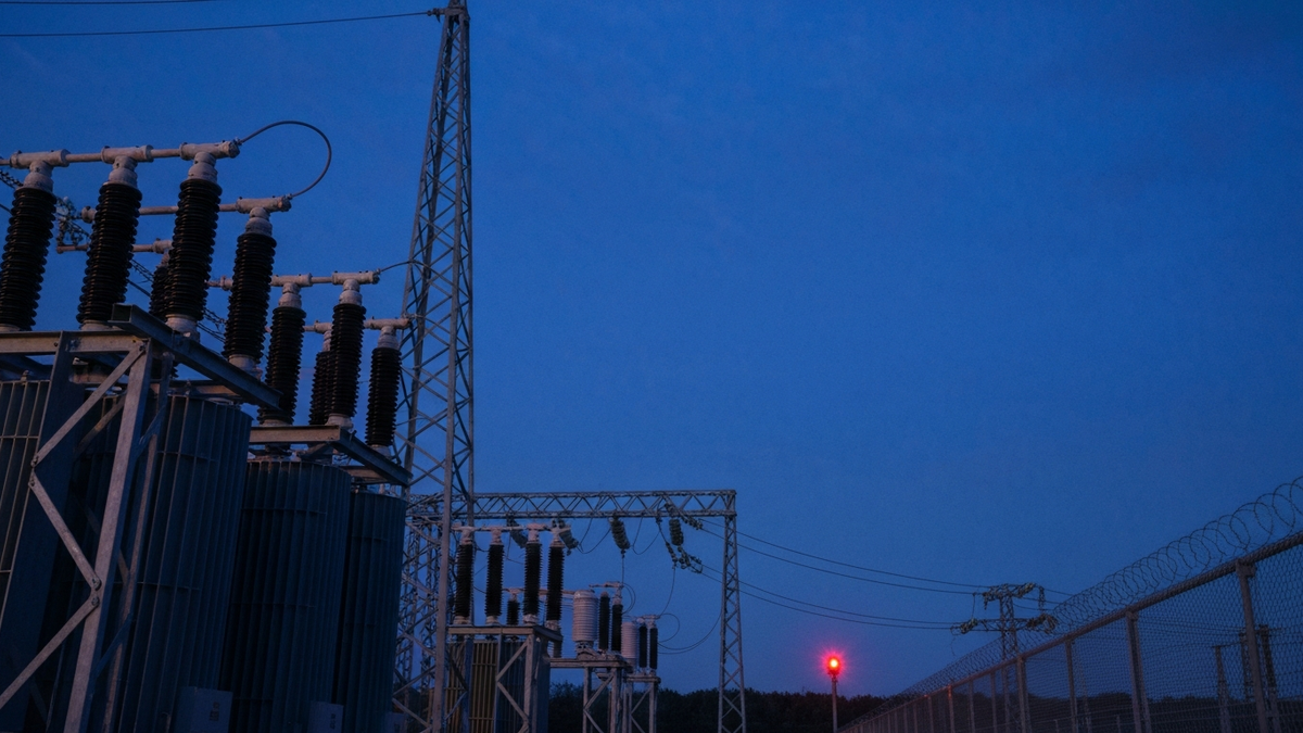 Electrical substation yard at blue hour, transformer banks and insulator stacks rising against a deep indigo sky