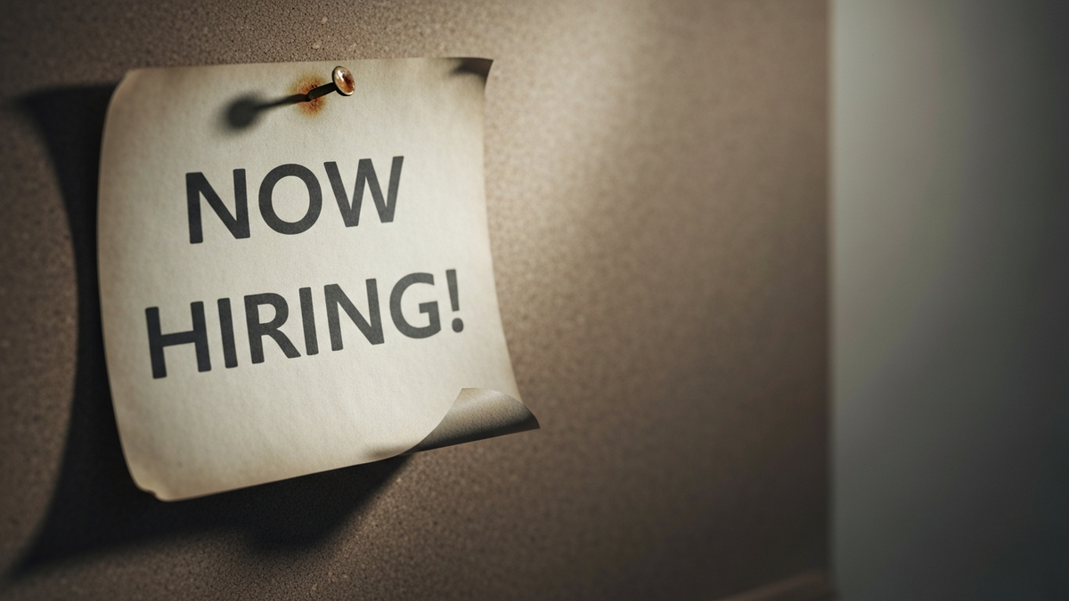 A faded Now Hiring sign on a near-empty cork board