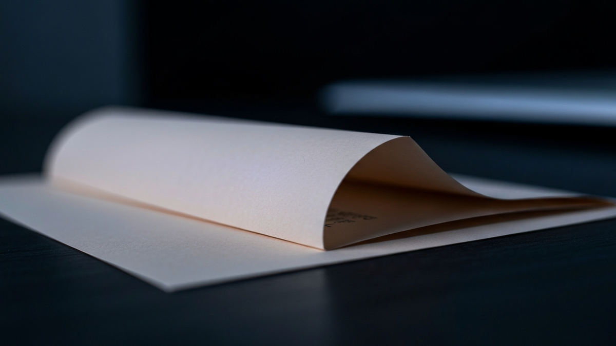 A folded corporate memo on cream paper lit dramatically on a dark desk, representing how layoff announcements are worded for workers.