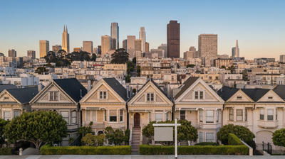 Aerial golden-hour view of San Francisco Victorian rooftops and downtown tech skyline with a blank real-estate sign