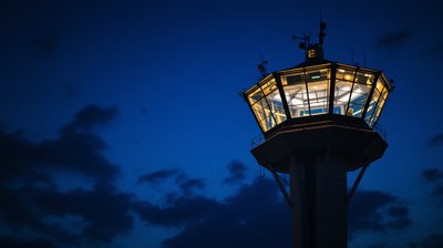 An airport control tower cab lit against a dusk sky
