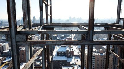 The unfinished steel frame of a high rise with city rooftops far below