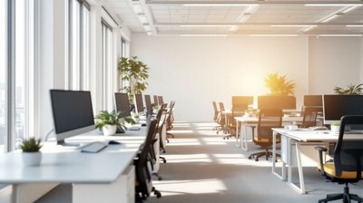 Rows of empty desks with monitors and black chairs in a sunlit open-plan office