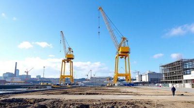 Two yellow shipyard gantry cranes above a cleared industrial building site on a sunny day