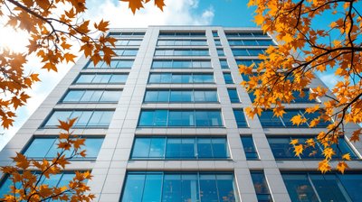 The glass and pale stone facade of a Dublin office headquarters framed by autumn leaves