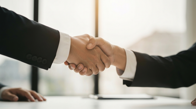 Two professionals shaking hands over a desk, evoking landing the job a strong resume earns.