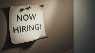 A faded Now Hiring sign on a near-empty cork board
