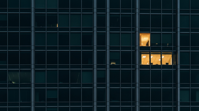 One warmly lit window in a dark office tower, evoking a resume that stands out and cannot be ignored.